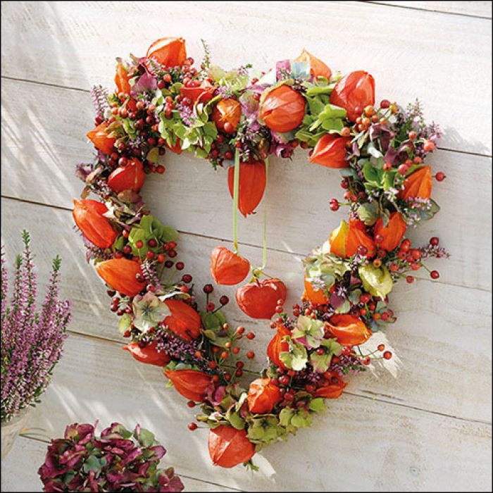 Servietten mit herzförmigem Herbstkranz aus Physalis, Beeren, Blüten und grünen Blättern auf hellem Holz