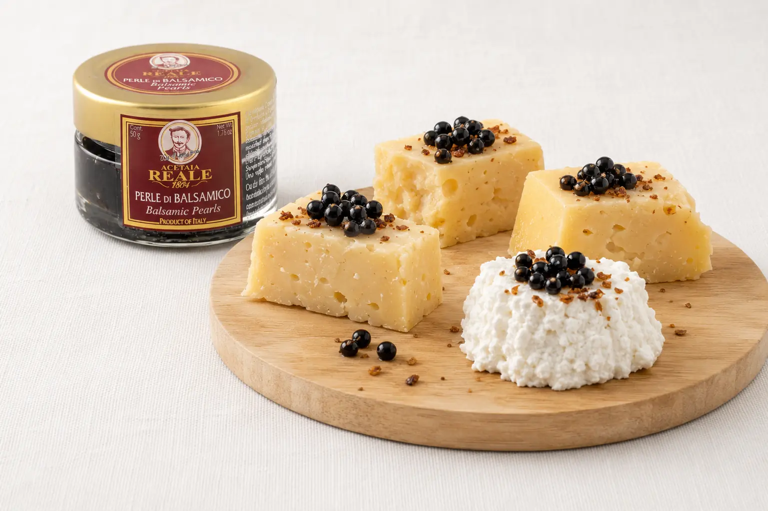 Acetaia Reale Balsamico Perlen mit Hartkäse und Frischkäse auf einem Holzbrett